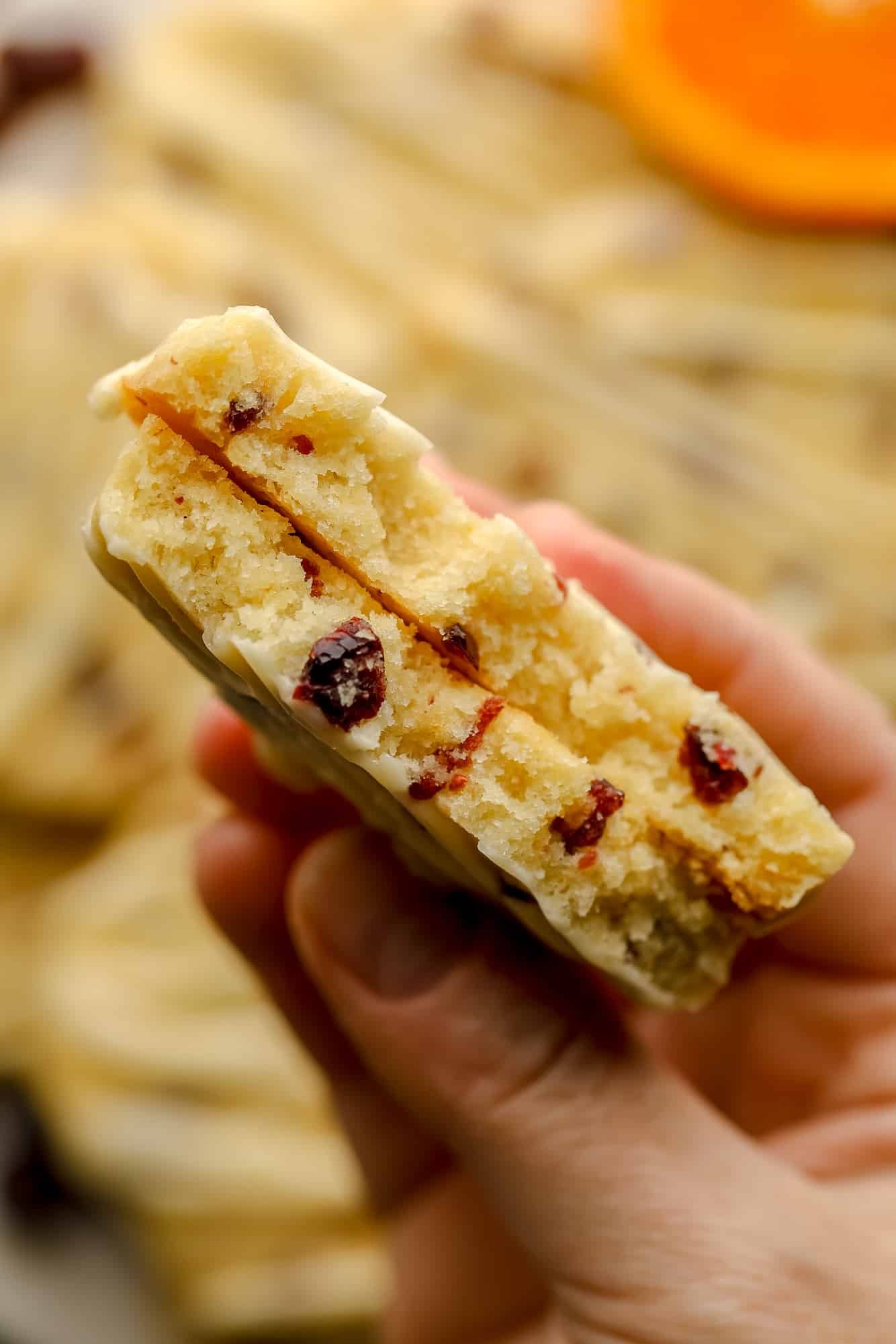 Uma mão da mulher segurando um biscoito laranja de biscoito de cranberry que foi cortado ao meio.