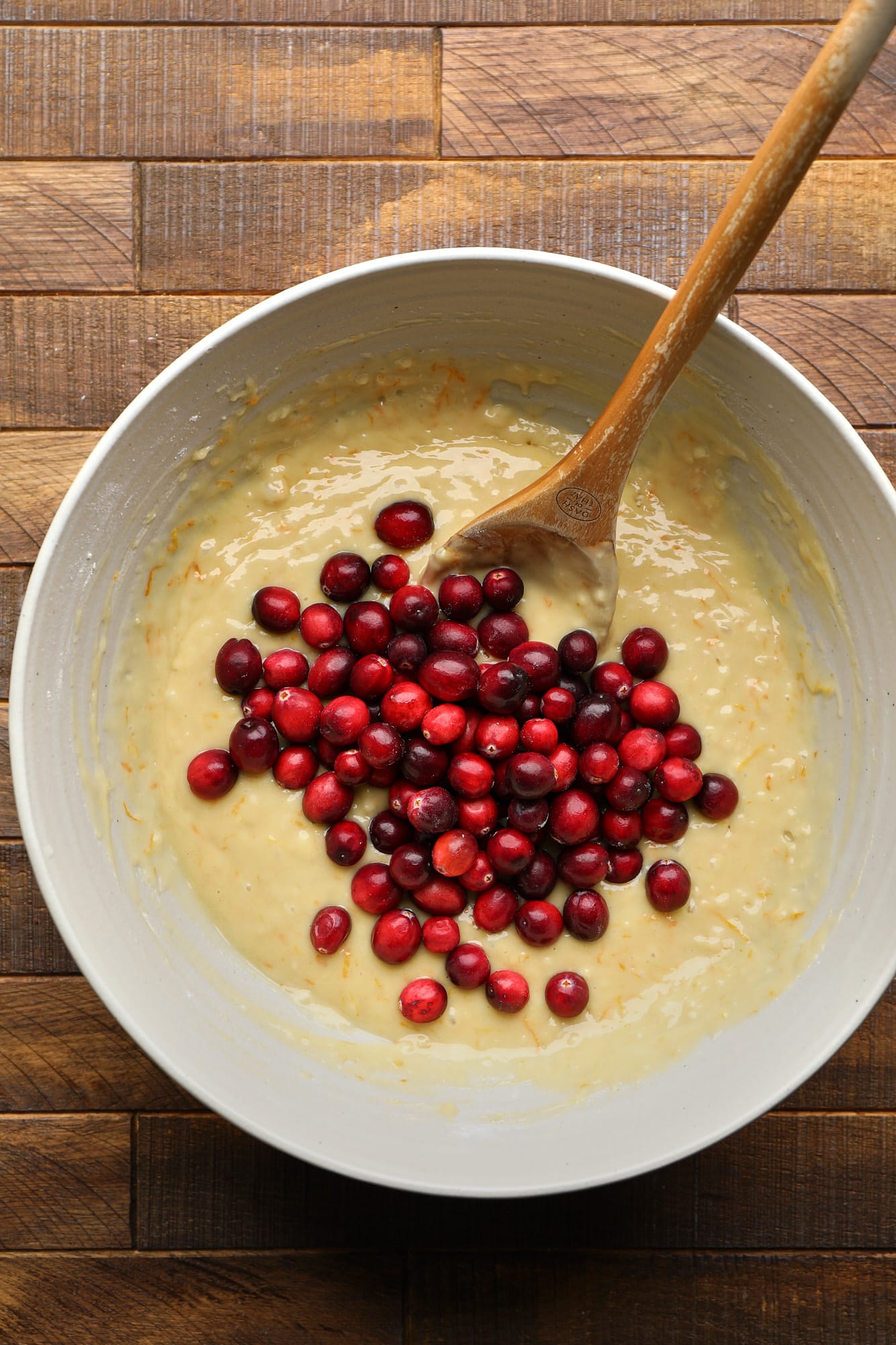 Usando uma colher de pau para dobrar os cranberries inteiros em massa de muffin.